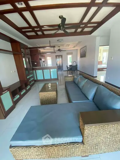 Spacious living room with stylish wicker furniture and modern ceiling design, perfect for relaxation.