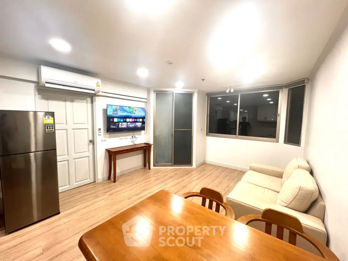 Modern living room with cozy sofa, dining table, and wall-mounted TV in bright apartment.