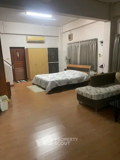 Spacious bedroom with modern furnishings and wooden flooring, featuring a cozy bed and ample natural light.
