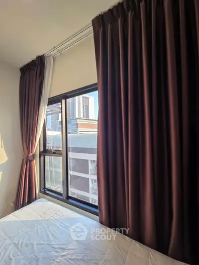 Cozy bedroom with large window and city view, featuring elegant dark curtains and natural light.