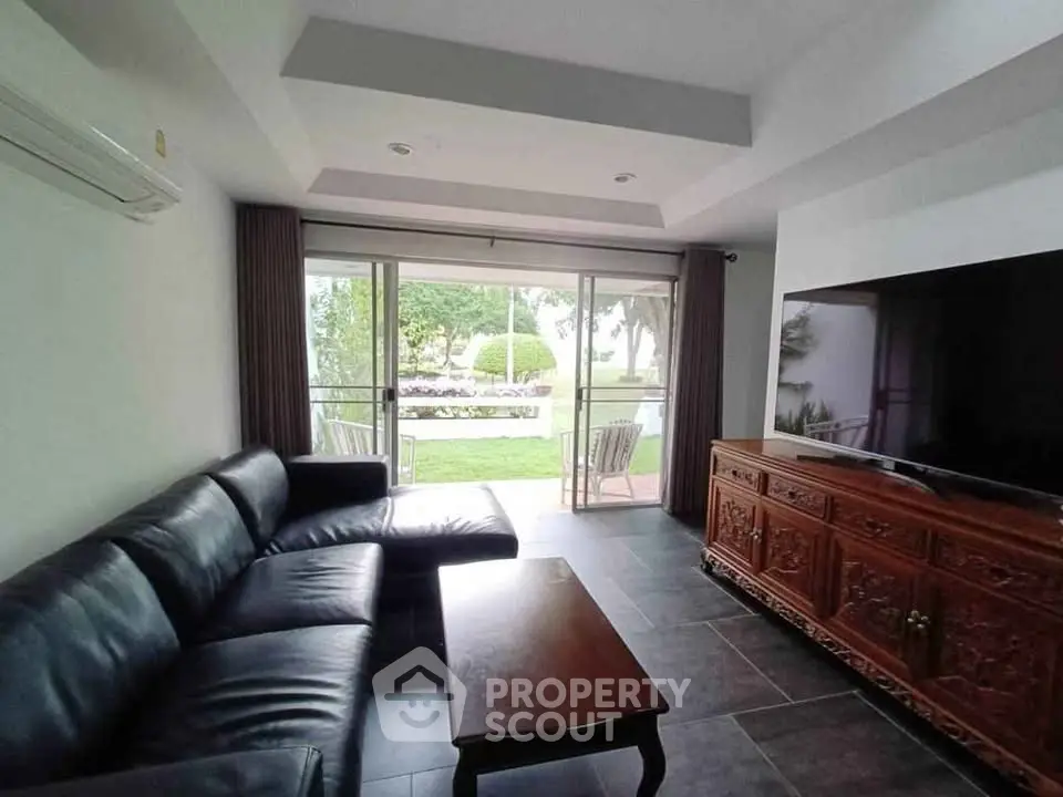 Spacious living room with garden view, featuring modern leather sofa and large flat-screen TV.