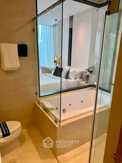 Luxurious bathroom with glass partition overlooking a stylish bedroom, featuring a modern bathtub and elegant decor.