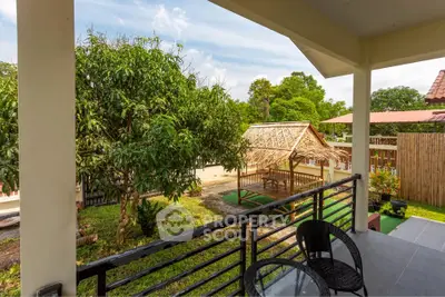 Charming balcony with outdoor seating overlooking lush garden and traditional gazebo.
