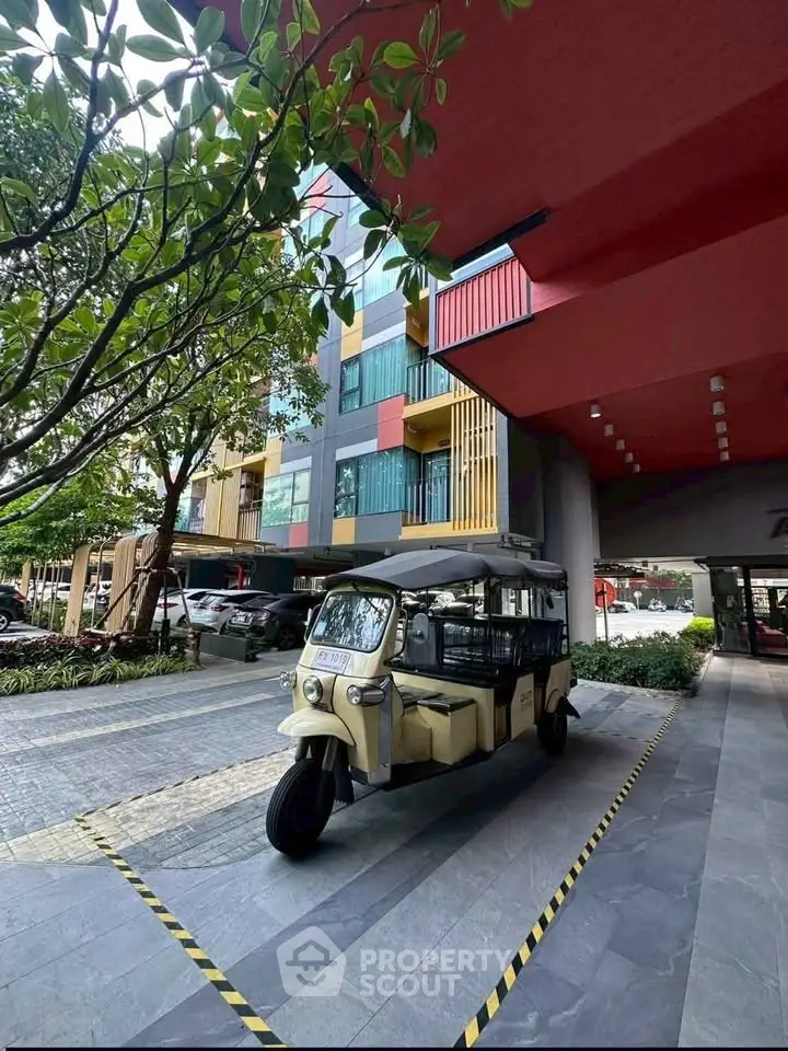 Modern building entrance with unique architecture and vibrant colors, featuring a tuk-tuk parked in front.