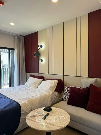Modern bedroom with stylish decor and cozy seating area, featuring elegant lighting and a glimpse of the balcony.