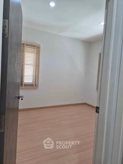 Spacious empty room with wooden flooring and natural light from windows.