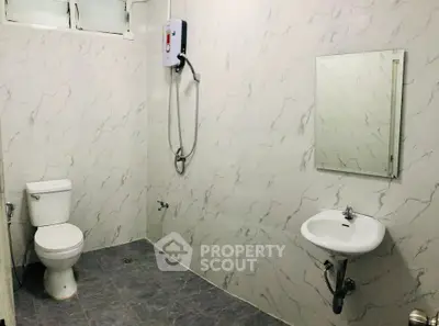 Modern bathroom with marble tiles, wall-mounted shower, and sleek fixtures.