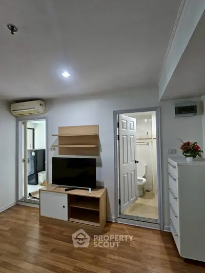 Modern apartment interior with wooden flooring, TV unit, and access to bathroom and bedroom.