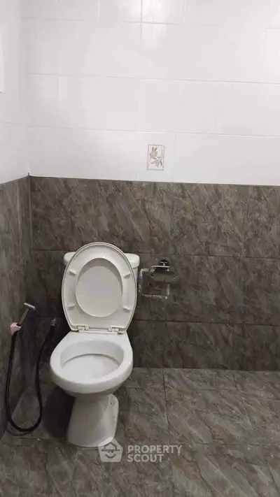 Simple bathroom with tiled walls and floor featuring a toilet and bidet spray.