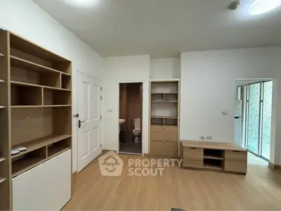Modern living room with wooden flooring and built-in shelves, featuring a glimpse of a compact bathroom.