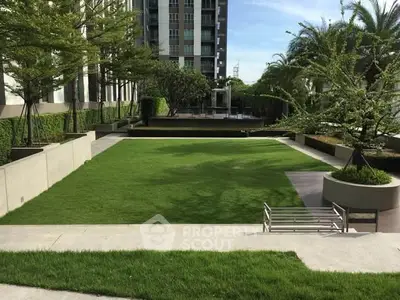 Lush green garden area in modern residential complex with seating and landscaped surroundings.