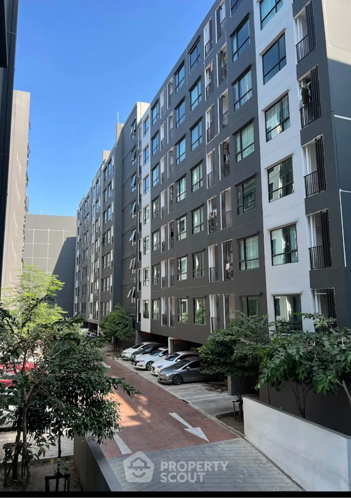 Modern urban apartment building with parking and lush greenery.