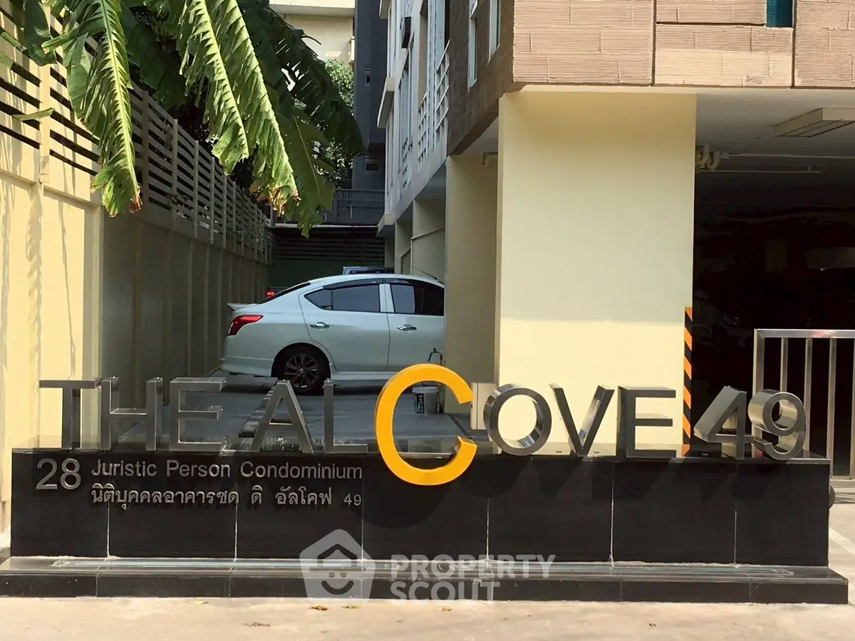 Modern condominium entrance with sleek signage and parked car, showcasing urban living.