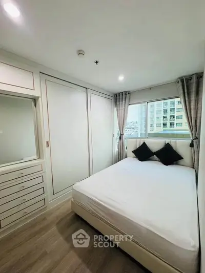 Modern bedroom with built-in wardrobe and large window offering city views.
