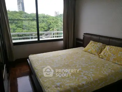 Cozy bedroom with large window offering lush green views in a modern apartment.