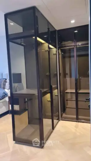 Luxurious walk-in closet with sleek glass doors and elegant lighting in a modern bedroom setting.
