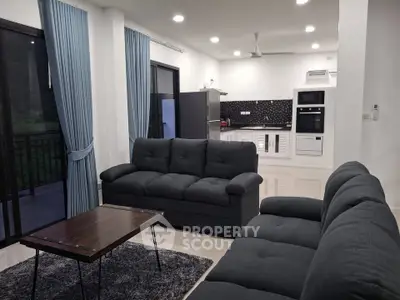 Modern living room with open kitchen, featuring sleek sofas and stylish decor.