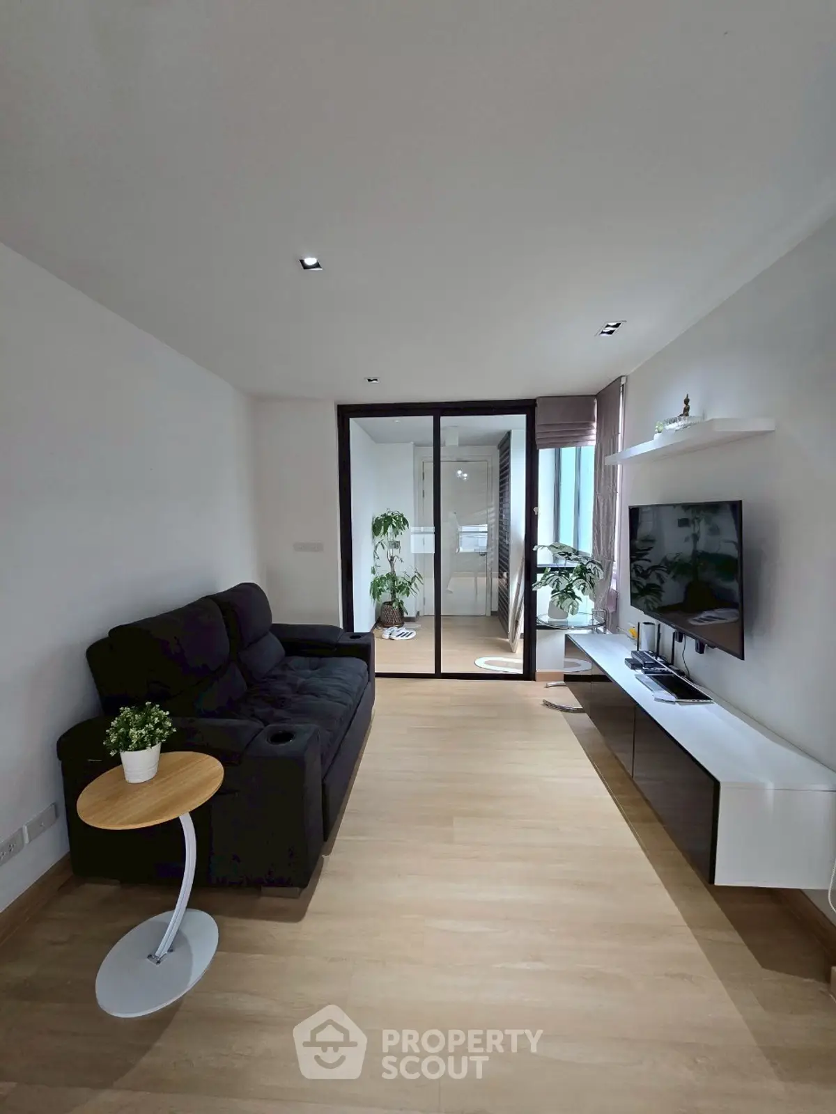 Modern living room with sleek black sofa and wall-mounted TV, bright and airy ambiance.