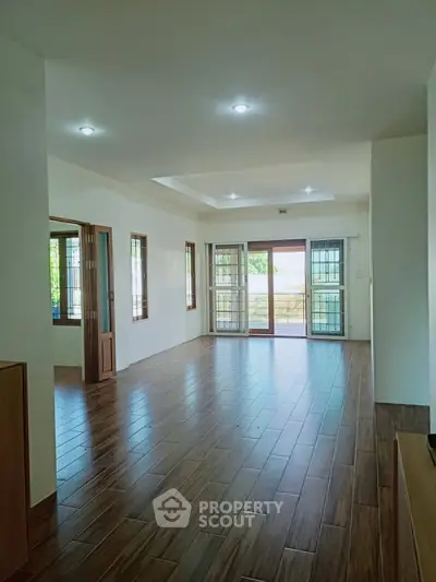 Spacious living room with wooden flooring and large windows for natural light.