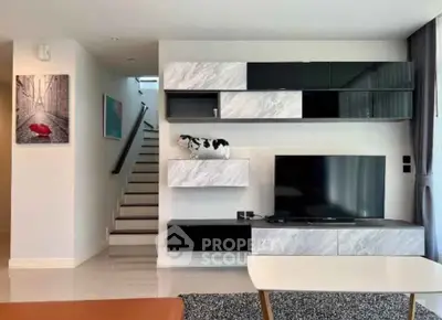 Modern living room with stylish TV unit and staircase, featuring sleek design and contemporary decor.