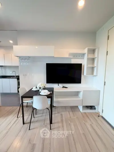 Modern living room with sleek TV setup and dining area in stylish apartment.