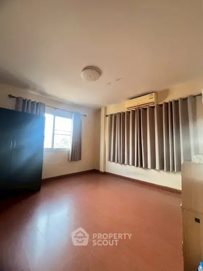Spacious bedroom with wooden flooring and ample natural light from large window.