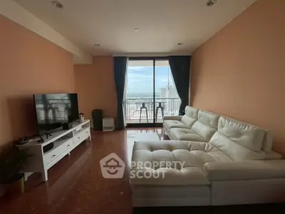 Spacious living room with white sectional sofa and large TV, featuring a stunning balcony view.