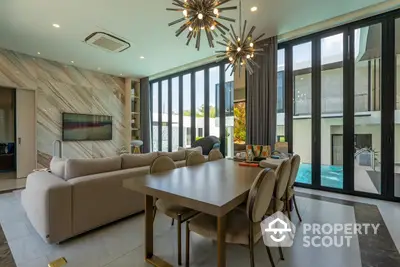 Luxurious open-plan living space with chic decor, floor-to-ceiling windows offering pool views, and a statement chandelier, perfect for upscale living.