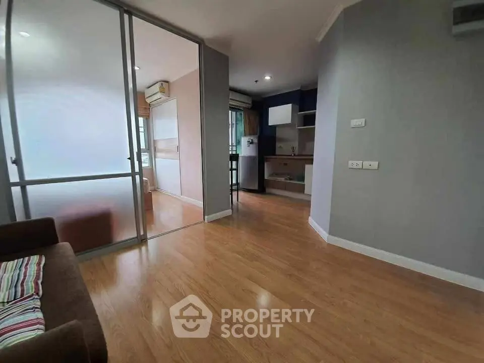 Modern apartment interior with wooden flooring and glass partition, featuring a compact kitchen area.