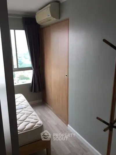 Cozy bedroom with wooden floor, window view, and air conditioning unit.