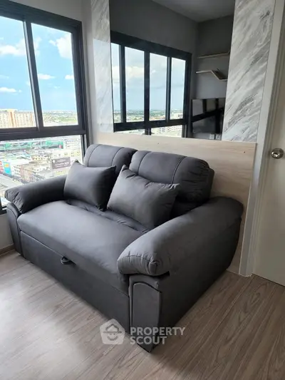 Modern living room with plush gray sofa and panoramic city view from large windows.