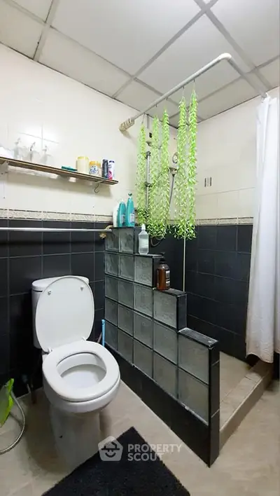 Cozy bathroom with modern shower and toilet, featuring stylish black and white tiles and decorative greenery.