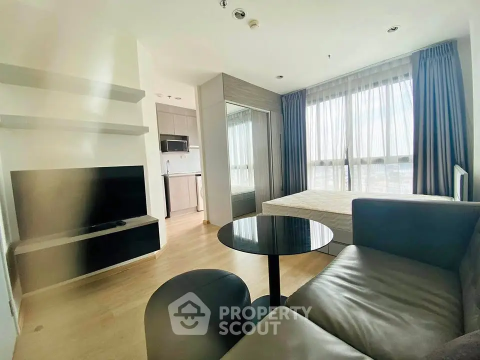 Modern studio apartment with open layout, featuring a cozy living area, sleek kitchen, and large window with natural light.