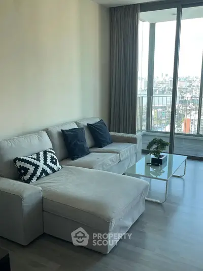 Modern living room with large windows and city view, featuring a stylish sofa and glass coffee table.