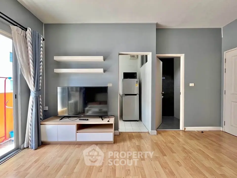 Modern living room with TV, shelves, and access to balcony and kitchen.