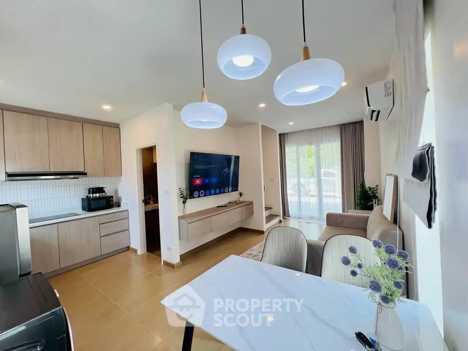 Modern open-plan living room with stylish kitchen and dining area, featuring elegant lighting and contemporary decor.