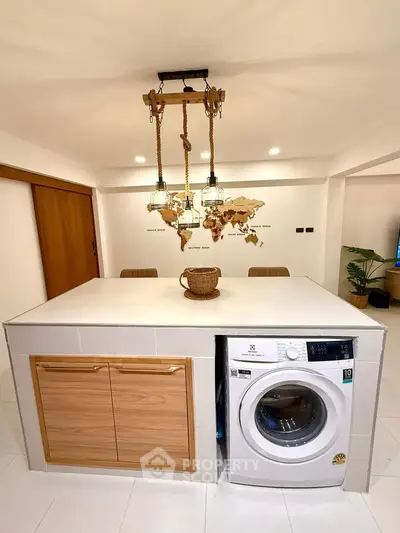 Modern kitchen with island, washing machine, and stylish pendant lights in a contemporary home.