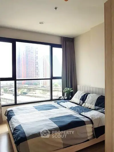 Modern bedroom with large window and city view, featuring stylish bedding and natural light.