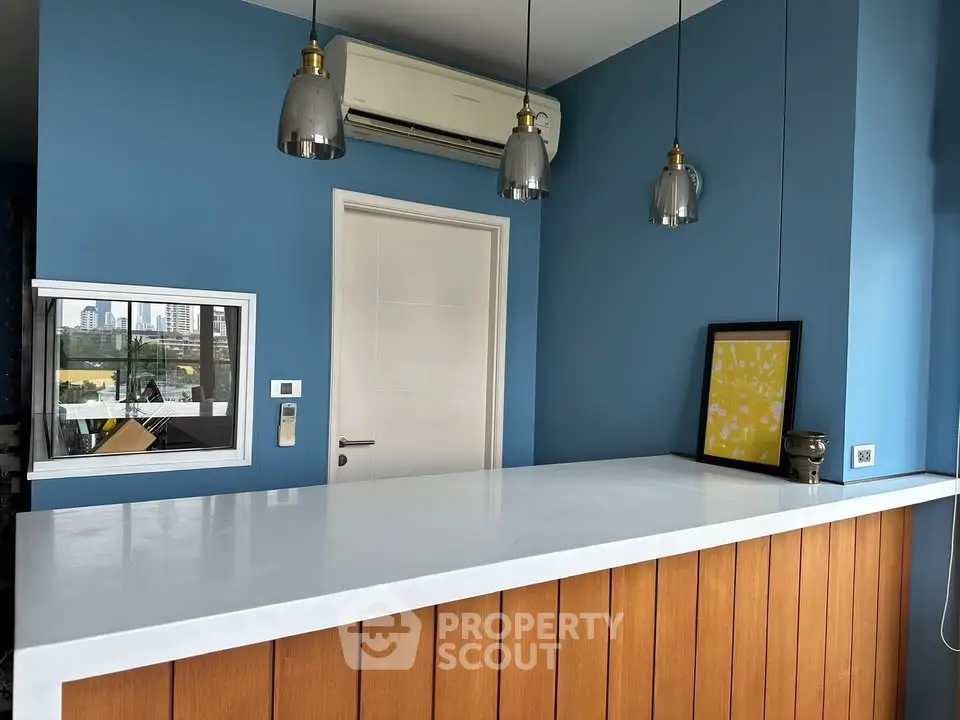 Modern kitchen with blue walls, wooden paneling, and sleek pendant lights