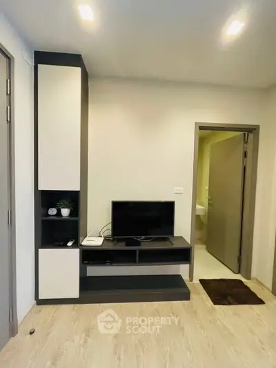 Modern living room with sleek TV stand and open door to bathroom, showcasing minimalist design.