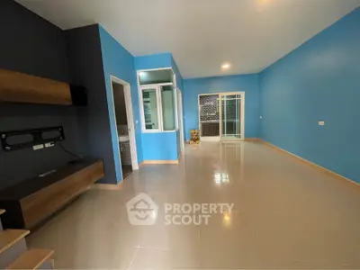 Spacious modern living room with blue walls and sleek tile flooring, featuring a built-in TV mount and large windows.