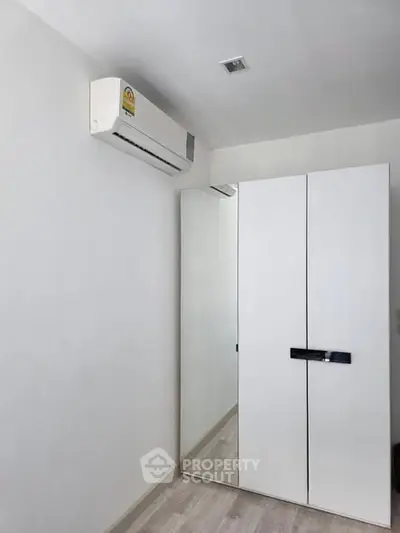 Modern minimalist bedroom with sleek wardrobe and air conditioning unit.