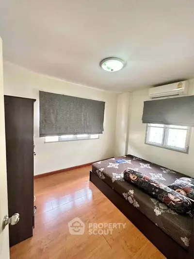 Cozy bedroom with wooden flooring, air conditioning, and ample natural light from two windows.
