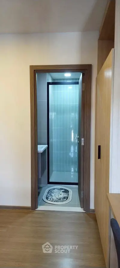 Modern bathroom entrance with sleek glass door and wooden flooring