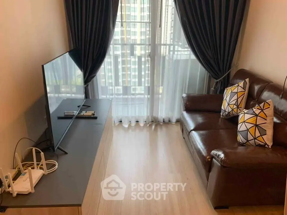 Cozy living room with leather sofa and large TV, featuring floor-to-ceiling windows and elegant curtains.