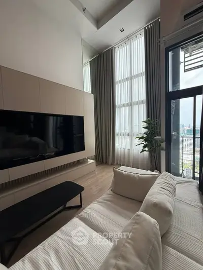 Modern living room with high ceilings and large windows offering city views.
