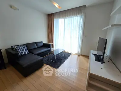 Modern living room with sleek black sofa, wooden flooring, and large window for natural light.