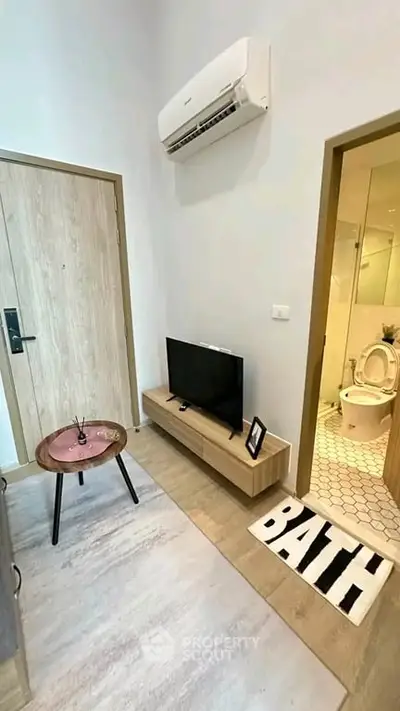 Modern compact living room with TV, air conditioning, and bathroom access in stylish apartment.