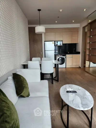 Modern living room with open kitchen, featuring sleek furniture and appliances.