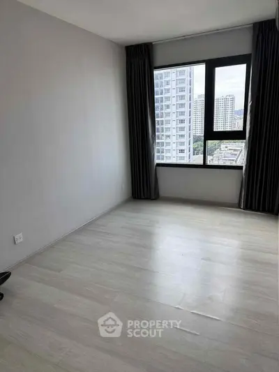 Spacious empty bedroom with large window offering city views in modern apartment.
